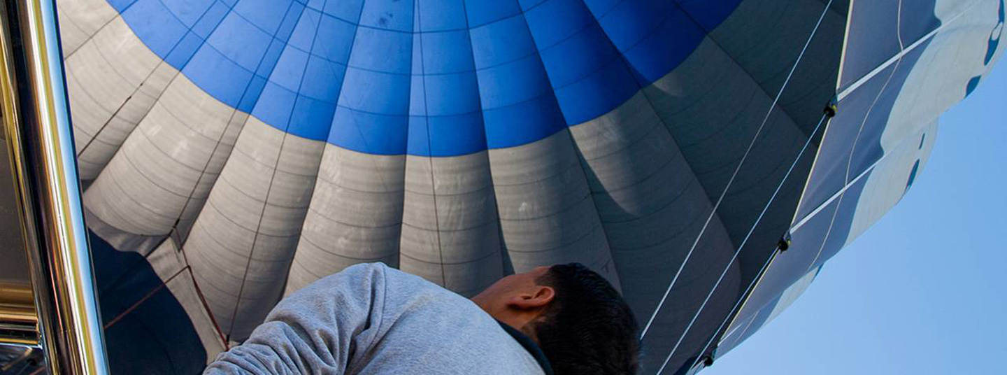 A skydiver wearing a red shirt maneuvers his yellow parachute near a modern building.